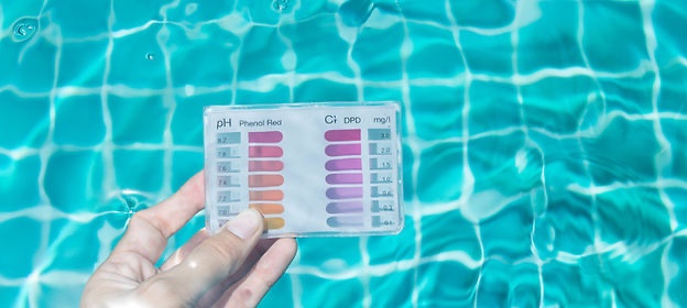 A hand holding a BioGuard chlorine and pH test card over a sunlit pool surface.