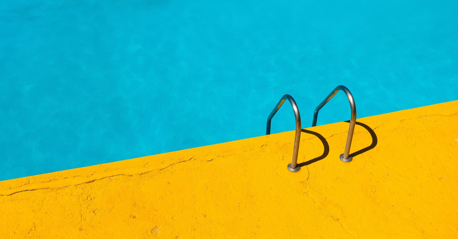 Turquoise pool water meeting a bright yellow concrete deck, with two silver ladder rails breaking the horizon — a Highland Pool & Spa installation in southern Illinois.