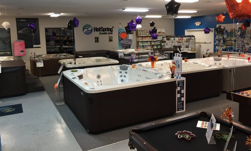Inside the Highland Pool & Spa showroom — a row of Hot Spring® spas on the floor, BioGuard chemistry on the back-wall shelves, and pool tables in the foreground.